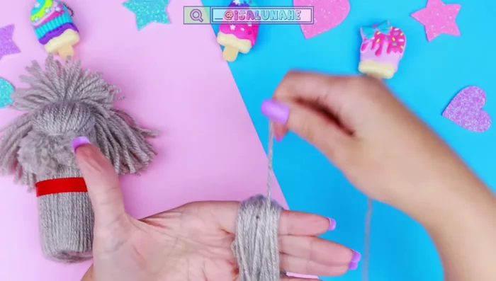 Hacer un pompón con 40 vueltas de lana, atarlo a la mitad, cortarlo y pegarlo en la parte posterior de la cabeza.