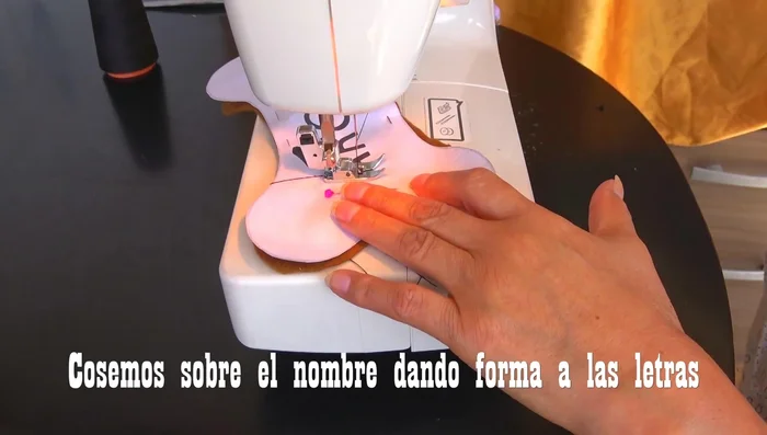 Coser el nombre: Coser el nombre sobre la tela usando una costura recta. Repetir la costura varias veces para que el hilo se vea más grueso y el nombre se destaque.