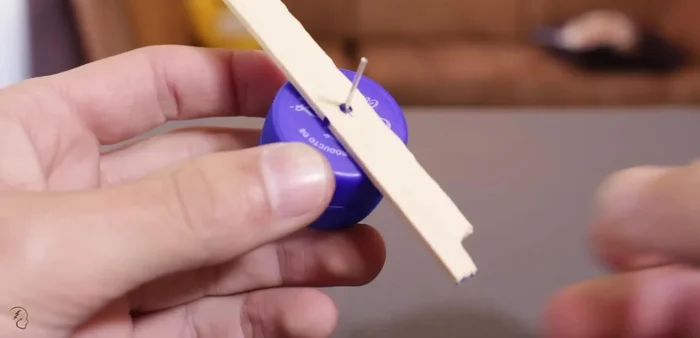 Pasar el palito de helado por el alambre, dejando un sobrante de alambre de aproximadamente 2 cm. Crear un pequeño gancho con este sobrante.