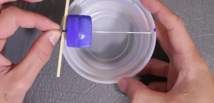 Pasar la otra punta del alambre por el agujero de la tapa blanca y pegar el palito de helado con silicona caliente para centrar la llanta.