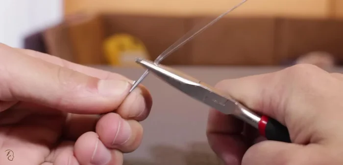 Enderezar un clip y cortarlo a la medida para el eje del juguete. Pasarlo por los agujeros de las tapas.