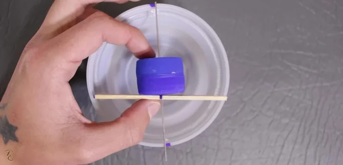 Pasar el palito de helado por el alambre, dejando un sobrante de alambre de aproximadamente 2 cm. Crear un pequeño gancho con este sobrante.