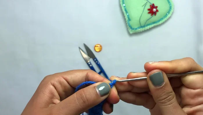 Introducir la aguja en el hueco de la esquina, pasar el hilo y cerrar el punto.