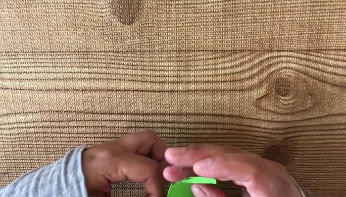 Doblar la tira de tela verde a lo largo y plancharla para marcar el doblez.