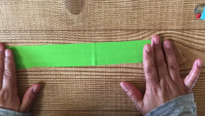 Doblar la tira de tela verde a lo largo y plancharla para marcar el doblez.