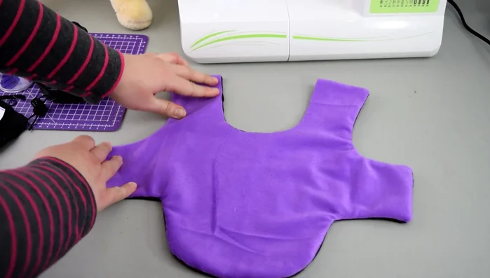 Dar Vuelta y Cierre: Gira la capa al derecho. Cierra la abertura, coloca 3 pedazos de elástico en puntos estratégicos (opcional) para sujetar la capucha. Pega el velcro a la capa.