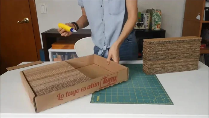 Preparar la caja: Aplicar resistol líquido en el fondo y paredes de la caja para asegurar que el bloque de cartones quede firmemente pegado. Colocar peso encima para que seque bien.