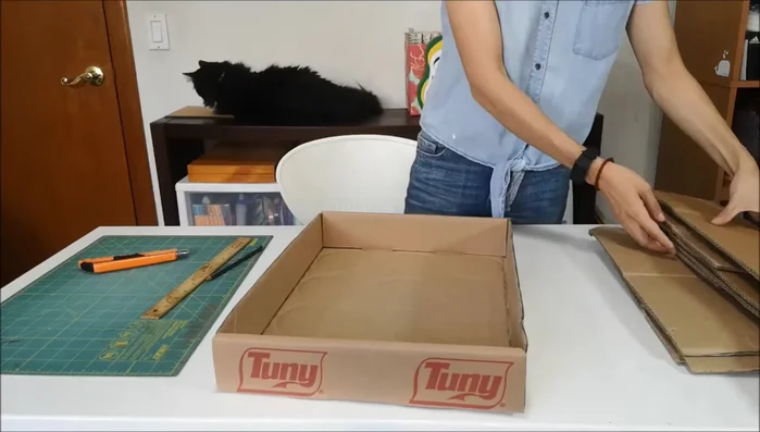 Medir la caja y cortar una muestra: Medir la caja de cartón (ejemplo: 6 x 32 cm en el vídeo) y cortar una muestra que servirá como molde para cortar rápidamente los cartones corrugados. Asegurarse que las canaletas del cartón corrugado queden verticales, cortando las tiras de forma horizontal.