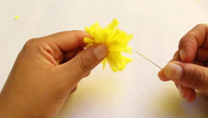 Introducir una aguja en la rafia para hacer el pompón más esponjoso.