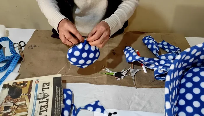 Crear la tira lateral: Medir el perímetro del cojín. Cortar una tira del material elegido (en el video se usa un acolchado plástico, pero se puede usar otra tela) con un ancho de 13 cm y una longitud igual al perímetro del cojín (aproximadamente 1.5 metros en este caso).