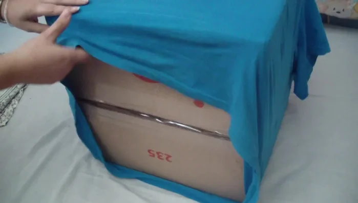 Fijar la camiseta: Grapar la parte trasera de la camiseta a la caja para asegurarla. Si la grapadora es pequeña, se puede usar más grapas para un mejor agarre. Si tienes una grapadora más grande, presiona la camiseta contra la caja para una fijación más segura.