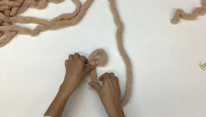 Iniciar la base circular: Poner la hebra sobre la mesa y pasarla por arriba haciendo una 'P'. Jalar la hebra sin apretar mucho. Sacar puntos flojos con tres dedos, formando tres hebras.