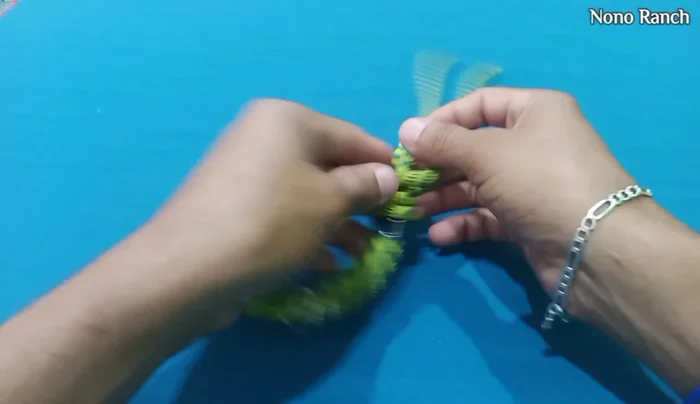 Introducir la tercera argolla en el nudo de cierre, pasando los dos extremos por la argolla y luego por el medio del collar. Hacer dos pasadas, asegurándose que la argolla esté en la posición correcta (ver video para detalles).