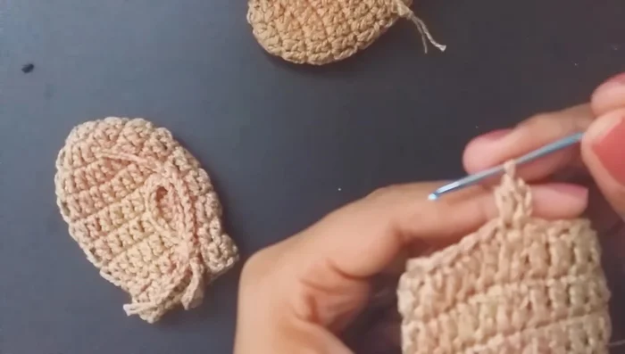 Crear el espacio para la cuerda: Subir 2 cadenas, tejer una media vareta, una cadena, saltar un punto base, tejer una media vareta en el siguiente punto alto. Repetir este patrón alrededor.