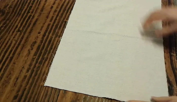 Preparación de la tela base: Tomar una tela tipo toalla, plegar una punta hacia arriba formando un triángulo y cortar sobre la línea vertical o diagonal para obtener dos triángulos.